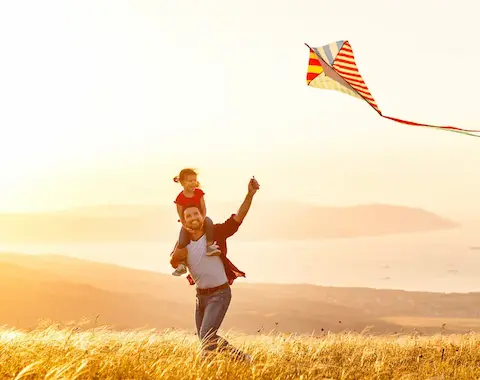 Un homme avec une fille sur ses épaules, un cerf-volant et un coucher de soleil.